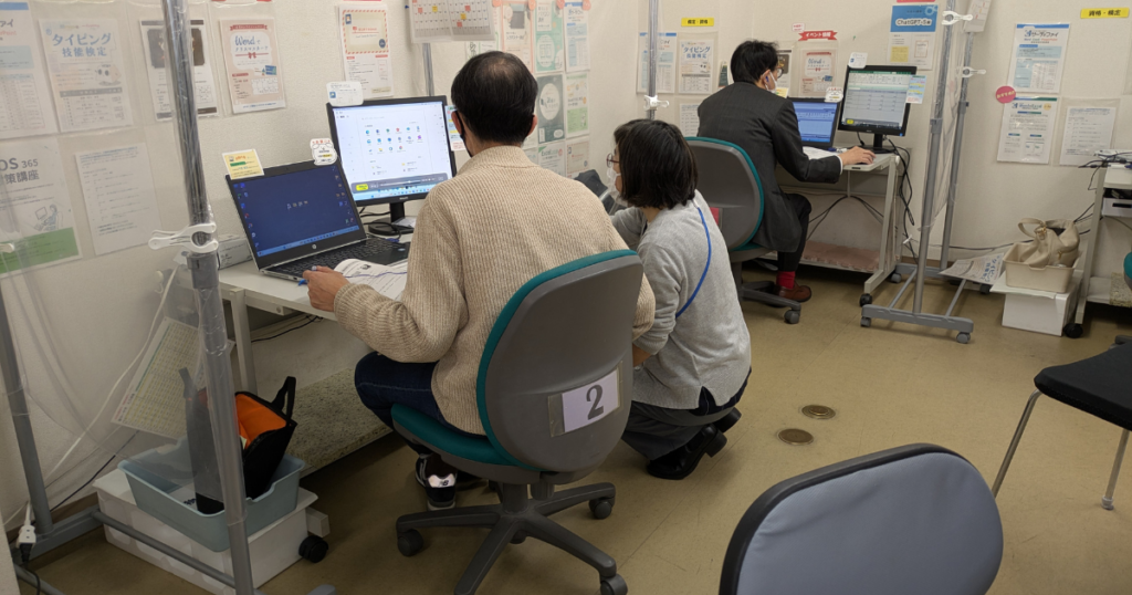 パソコン教室で講師が受講者の操作をサポートしている様子